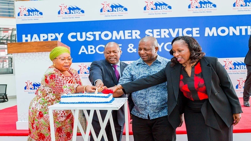 NBC Bank Managing Director Theobald Sabi (2nd-L), leads bank's Chief Operating Officer, Alelio Lowassa (R), along with long-standing customers, including Zuhura Maganga (L) and Asaa Simba, in cutting a special cake as a symbol of the launch