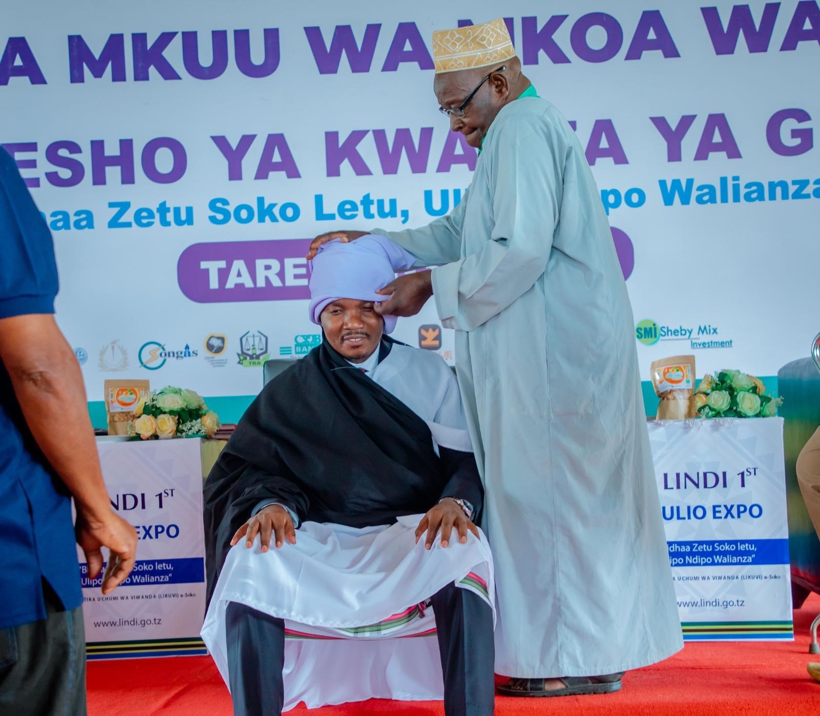  Lindi Region elder Abdallah Livembe dresses Industry and Trade minister Dr Selemani Jafo in traditional attire during the launch of an agricultural exhibition in the southern region at weekend. 