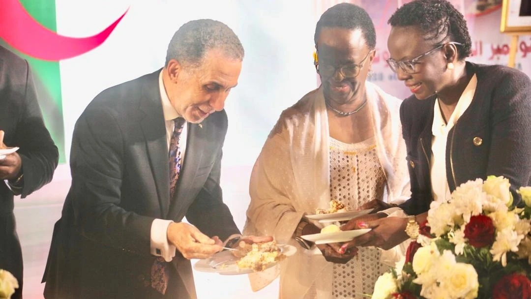 Algerian Ambassador to Tanzania Ahmed Djellal (left) placing a piece of cake to former Minister of Foreign Affairs and East African Cooperation, Liberata Mulamula (centre).