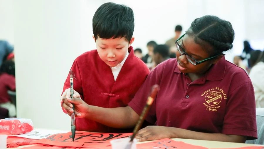 A student from Beijing teaches a student from Medgar Evers College Preparatory School of New York to practice Chinese calligraphy during a culture exchange event in New York, the United States, Feb. 2, 2018. 