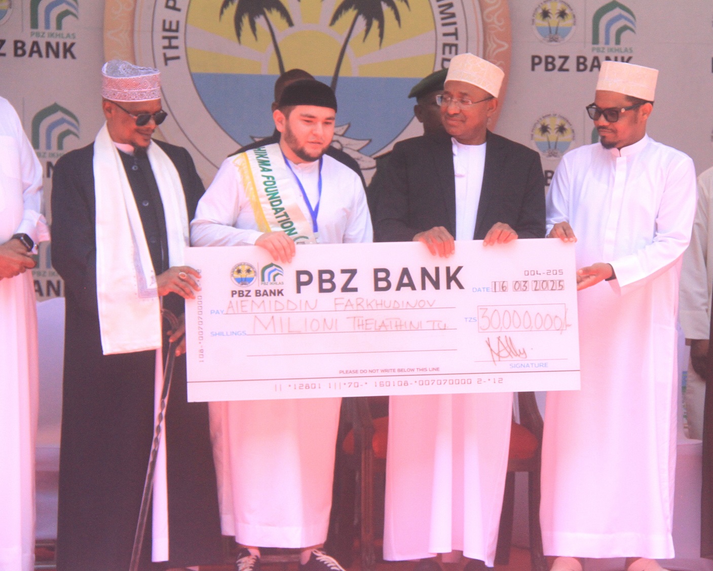 Zanzibar President Dr. Hussein Mwinyi (2nd R), presents a dummy cheque to the winner of the largest Quran recites competition in the world, Aiemidddin Farkhudinov from Russia held at the Benjamin Mkapa Stadium in Dar es Salaam on Sunday. 