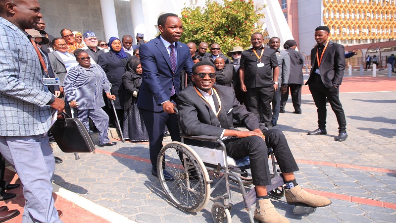 Patrobas Katambi, Deputy Minister of State in the Prime Minister’s Office (Labour, Employment, Youth and Persons with Disabilities), assists a person with disability who was on a visit to the National Assembly in Dodoma city yesterday. 